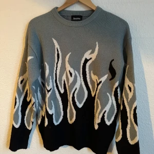 Grå tröja med flammönster från Bershka - Snygg grå tröja från Bershka med ett coolt flammönster i svart och vitt. Perfekt för att sticka ut i mängden. Tröjan har långa ärmar och en rund halsringning. Oversize