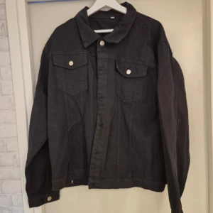 Svart jeansjacka med tryck - Cool svart jeansjacka med ett färgglatt tryck på ryggen som säger 'The Dream is true'. Jackan har knappar framtill och två bröstfickor med lock. Perfekt för en avslappnad stil med en unik touch.