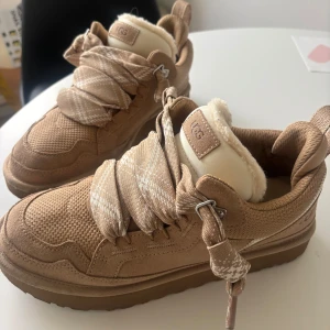 Sand sneakers från UGG - Säljer ett par snygga beige sneakers från UGG med fluffigt foder och breda snören. Skorna har en robust sula och är perfekta för kyligare dagar. De är både stiliga och bekväma. Färg Sand