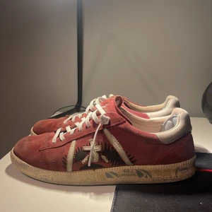 Premiata skor - Snygga röda sneakers i mocka med vita snören och en unik broderad detalj på sidan. Perfekta för en avslappnad stil. Dessa premiatas går nypris för cirka 3000 men mitt pris 1899, priset är ej hugget i sten och går ner i snabb affär, skick 7,5/10 hör av er!