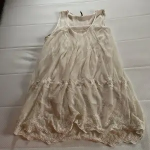 Säljer en superfin beige klänning från Soyaconcept. Den är ärmlös och har vackra spetsdetaljer längst ner. Perfekt för sommardagar eller en avslappnad fest. Materialet känns lätt och luftigt, vilket gör den bekväm att bära hela dagen. Har kort längd ner till knänna max. 