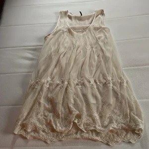 Beige ärmlös klänning från Soyaconcept - Säljer en superfin beige klänning från Soyaconcept. Den är ärmlös och har vackra spetsdetaljer längst ner. Perfekt för sommardagar eller en avslappnad fest. Materialet känns lätt och luftigt, vilket gör den bekväm att bära hela dagen. Har kort längd ner till knänna max. 
