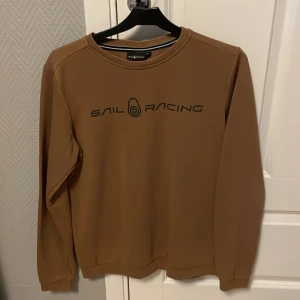 Brun tröja från Sail Racing - Säljer en snygg brun tröja från Sail Racing i storlek 170. Den har en stilren design med svart text på bröstet. Perfekt för både vardag och lite mer avslappnade tillfällen. Tröjan är i mycket bra skick och redo för en ny ägare!