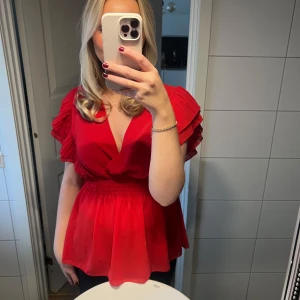 Röd blus med volangärmar - Säljer en superfin röd blus med volangärmar och omlott-design. Den har en smickrande passform med resår i midjan som ger en fin siluett ❤️