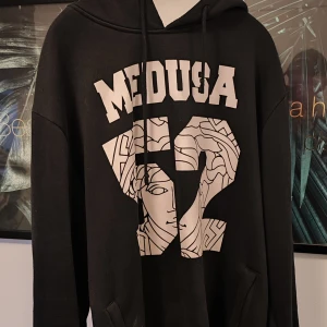 Svart hoodie med Medusa-tryck - Säljer en svart hoodie med coolt Medusa-tryck på både fram- och baksidan. Den har en stor luva och är perfekt för en avslappnad stil. Passar bra till både jeans och joggers!