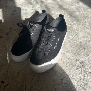 Svarta skor calvin klein - Svarta tygskor med snörning och vit sula. Från calvin klein. Använt fåtal gånger. Sköna att gå i och luftiga! Stl 37