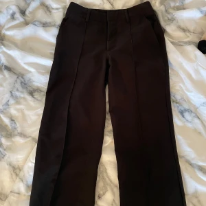 Svarta kostymbyxor - Snygga svarta byxor, mid waist med pressveck i mycket bra skick.  Använt några gånger men är tyvärr för stora för mig i midjan. Nypris 599kr