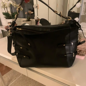 Svart handväska  - Säljer denna jättefina väskan som ser nyköpt ut! Köpt från arkivet förra väckan för 400 kr. Väskan är svart och har lite silvriga och guldiga detaljer😍 Rymlig och perfekt till skolan!  Öppen för prisförslag men tryck gärna på ”köp nu”, postar snabbt!