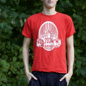 Röd t-shirt med Lund Super Bowl 2024 tryck - Säljer en röd t-shirt med tryck för Lund Super Bowl 2024. Den är kortärmad och i bomull, perfekt för vardagsbruk eller sportiga aktiviteter. T-shirten har en normal passform och är i bra skick. Perfekt för dig som gillar unika tryck och sportevenemang!