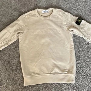 Beige Stone Island Tröja - Säjer en snygg beige tröja från Stone Island, den är i nytt skick och endast använd några få gånger. Tröjan är i storlek Junior och passar för folk som är runt 12 år gamla. Modellen görs ej längre vilket gör den ännu mer exklusiv😉Nypris var 2099kr på NK✅
