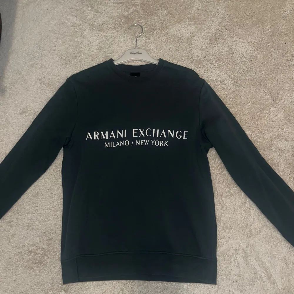 Säljer en stilren mörkgrön sweatshirt från Armani Exchange med texten 'Milano/New York' på bröstet. Tröjan har en klassisk passform och är perfekt för både vardag och avslappnade tillfällen. Den är i bra skick och superbekväm att ha på sig. Passar perfekt till jeans eller joggers!. Tröjor & Koftor.