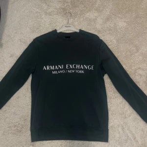 Mörk grön sweatshirt från Armani Exchange - Säljer en stilren mörkgrön sweatshirt från Armani Exchange med texten 'Milano/New York' på bröstet. Tröjan har en klassisk passform och är perfekt för både vardag och avslappnade tillfällen. Den är i bra skick och superbekväm att ha på sig. Passar perfekt till jeans eller joggers!