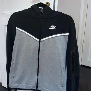 Nike Tech Fleece Full-Zip hoodie - Säljer en svart och grå Nike Tech Fleece Full-Zip huvtröja. Juniorstorlek 158-170. Material: 53% bomull, 47% polyester Ej avtagbar huva
