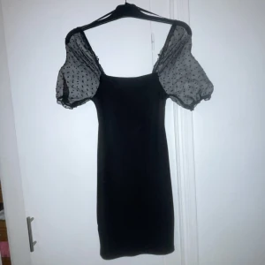 Svart klänning med prickiga puffärmar - Elegant svart klänning med transparenta puffärmar i prickigt mönster. Perfekt för en stilren look med en touch av lekfullhet.
