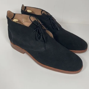 Svarta mocka boots från H London - Snygga svarta boots i mocka från H London med snörning och en stilren design. Perfekta för en elegant look med en robust sula i brunt läder.