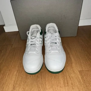 Vita och gröna sneakers från New Balance - Snygga vita sneakers från New Balanceb med gröna detaljer. Skorna har snörning och en bekväm sula, perfekt för en stilren look. Skorna var köpta för inte så länge sen och har tyvärr blivit för små. Skorna var köpta för 1350kr.  Priset kan diskuteras vid snabb affär 