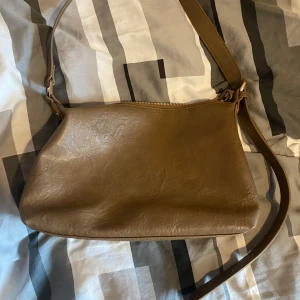 Brun väska  - Söt brun väska säljes! Var min favorit länge men har inser att jag har för många väskor hemma. Man kan ändra storleken på bandet! Har sytt fast kedjan men är inte något som syns så mycket och påverkar ej användning! 