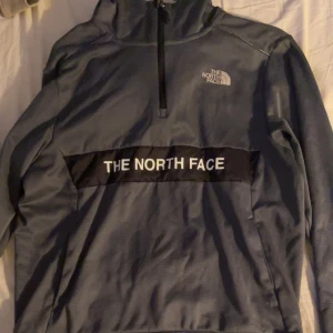 Grå tröja från The North Face - Säljer en grå tröja från The North Face med halv dragkedja och logga på bröstet. Tröjan har långa ärmar och en stor logga över bröstet. Perfekt för kyliga dagar. Oanvänd storlek M