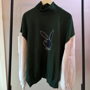 Grön och vit tröja från Playboy x Missguided - Snygg grön och vit tröja från Playboy x Missguided med en stor Playboy-logga och siffran 53 på baksidan. Tröjan har en hög krage och långa ärmar i kontrasterande färg. Perfekt för en avslappnad stil.