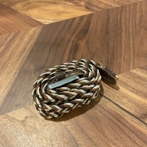 Flätat bälte med bruna detaljer - Snyggt flätat bälte i beige och brunt med en stilren silverfärgad spänne. Perfekt för att ge din outfit en extra touch. Bältet har bruna skinnändar som ger en klassisk look.