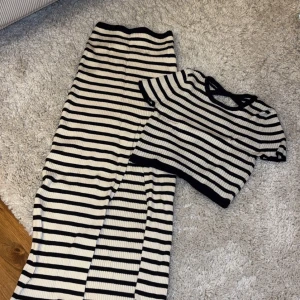 Randig ribbad set med kjol och topp - Snygg ribbad topp och kjol med svart och vit randigt mönster. Toppen har korta ärmar och en rund halsringning. Perfekt för en stilren look.