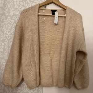 Beige stickad kofta från Lindex - Mysig beige stickad kofta från Lindex. Perfekt för kyliga dagar med sin öppna design och långa ärmar. Enkel att matcha med olika outfits.