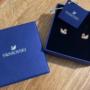 Rosegold-örhängen från Swarovski - Eleganta örhängen i form av svanar från Swarovski. De är guldiga och dekorerade med glittrande stenar som ger en lyxig känsla. Perfekta för att lägga till en touch av glamour till din look. Aldrig använda. 😉
