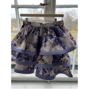 Blommig kjol från Elisabetta Franchi - Säljer en vacker blommig kjol från Elisabetta Franchi i lavendelfärg. Kjolen har volanger och ett härligt mönster som ger en romantisk känsla. Perfekt för speciella tillfällen. Helt ny med prislapp kvar. Italiensk storlek 42, motsvarande svensk 38