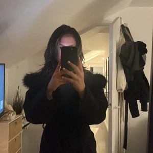 Svart kappa med pälskrage - Snygg svart kappa med en lyxig pälskrage. Perfekt för kyliga dagar och ger en elegant touch till din outfit. Den har långa ärmar och en klassisk passform.