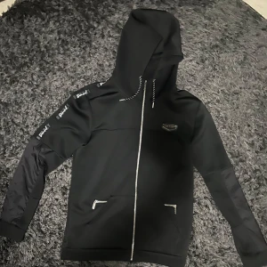 Supply & Demand zip hoodie  - Snygg svart hoodie från Supply & Demand med dragkedja och huva. Den har vita detaljer och logotyp på armarna. Storlek L men passar även XL, säljer då det inte är min stil längre.