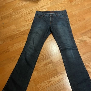 Blå lågmidjade jeans från Zoul - Snygga blå utsvängda jeans från Zoul med klassisk femficksdesign och orange sömmar. Perfekta för en avslappnad stil. De har en knapp och dragkedja framtill.