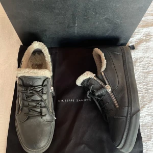 Giuseppe Zanotti Frankie  - Snygga svarta sneakers i skinn från Giuseppe Zanotti med dragkedja och snörning. Skorna är mysigt fodrade, perfekt för kyligare dagar. Stilren design med robust sula. Del av löparen saknas (bild 5), men påverkar inte användningen. Vid övriga frågor är det bara att höra av sig 📩
