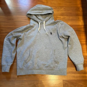 Grå hoodie från Ralph Lauren - Säljer en klassisk grå hoodie från Ralph Lauren med en broderad logga på bröstet. Köpt på Plick av en försäljare som ljög om skicket. Tex fick jag hem tröjan med avklippta snören. Säljer denna för en liten peng bara av rent behov att bli av med den. Hör av dig för fler funderingar!
