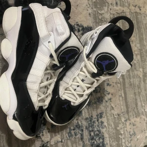 Nike Air Jordans i svart och vit samt Royal blue  - Snygga Nike Air Jordans i svart och vit med Royal blue detaljer. Skorna har en hög design med snörning och en unik sula. Perfekta för dig som vill ha en stilren och sportig look. Storlek 37,5 men själv har jag 36,5 och de passar mig bra. De köptes för ca 200 euros. 