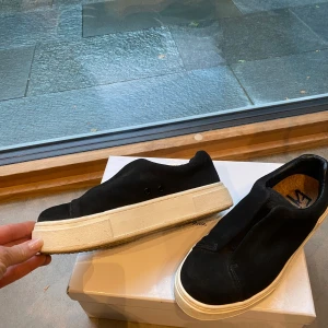Svarta sneakers i mocka - Snygga svarta sneakers i mocka med vit sula. De har en stilren design utan snörning, vilket gör dem enkla att ta på och av. Perfekta för en avslappnad stil.