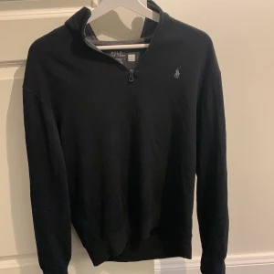Svart tröja med dragkedja från Polo Ralph Lauren - Säljer en stilren svart tröja från Polo Ralph Lauren med halv dragkedja och broderad logga på bröstet. Perfekt för en avslappnad men snygg look. Storlek s
