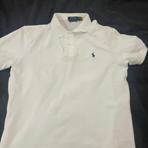 Polo Ralph Lauren pike  - Säljer en klassisk vit pikétröja från Ralph Lauren i custom slim fit. Tröjan har en broderad logga på bröstet och knappar vid kragen. Perfekt för en stilren look. Priset går alltid att diskutera vid snabb affär 