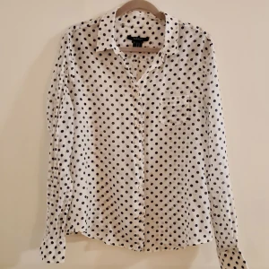 Vit prickig skjorta från GANT - Snygg vit skjorta i silke/bomulls blandning från GANT med svarta prickar. Skjortan har långa ärmar och knappar framtill och är tunn och silkig. Perfekt för en klassisk look. Nypris 1895.
