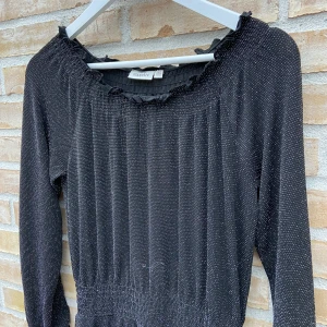 Svart glittrig klänning från KappAhl🌟 - Snygg svart klänning från KappAhl med glittrigt mönster. Klänningen har långa ärmar och en elastisk midja för en bekväm passform. Perfekt för festliga tillfällen som nyår!