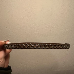 Brunt pannband med kedjedetaljer - Snyggt brunt pannband med unika silvriga kedjedetaljer. Storlek full, i nyskick