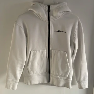 Vit hoodie från Sail Racing - Säljer en stilren vit hoodie från Sail Racing med dragkedja och två stora fickor framtill. Perfekt för en avslappnad look. Hoodien har långa ärmar och en bekväm passform.