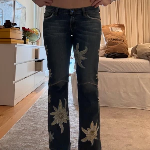 Blå jeans med blommigt mönster - Snygga blå jeans med stora målade blommor i vitt och gult. Byxorna har en bootcut-stil och är lågmidjade🥰. Märke är bigstar. SÅÅÅ UNIKA!!