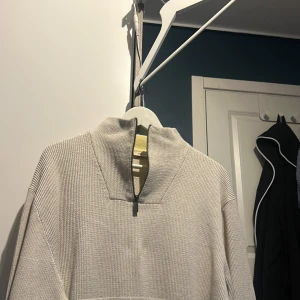 Beige stickad tröja från Esprit - Säljer en stilren beige stickad tröja från Esprit med dragkedja vid halsen. Perfekt för kyligare dagar med sin mjuka och bekväma passform. Tröjan har långa ärmar och en hög krage som ger extra värme.
