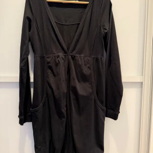 Svart make a wish cardigan - Snygg svart lång kofta i mjuk och elastisk bomull. En mjuk resår som markerar midjan fint. En metallhylsa framtill som man stänger koftan med. V-ringning och långa ärmar. Den har en subtil broderad detalj på ryggen och praktiska fickor framtill. Perfekt för en stilren look. Endast använd vid ett tillfälle så i mycket fint skick.