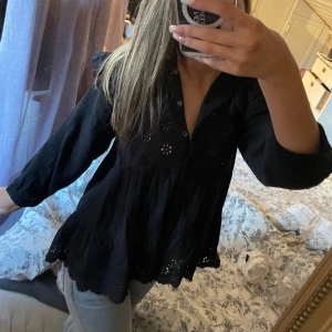 Svart blus med broderade detaljer - Säljer en svart blus med v-ringning och knappar framtill. Blusen har fina broderade blommor. Perfekt för en stilren look. Märket är part two och den är köpt för ca 800-700kr säljer för 400kr! Den är använd en gång, den har inga defekter eller fläckar. Storlek 36! Klicka gärna på köp nu!