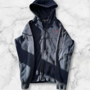 Mörkblå hoodie från U.S. Polo Assn. - Säljer en mörkblå hoodie från U.S. Polo Assn. med dragkedja och broderad logga i rött på bröstet. Perfekt för en avslappnad stil. Den har långa ärmar och en bekväm huva.           Pris kan diskuteras!