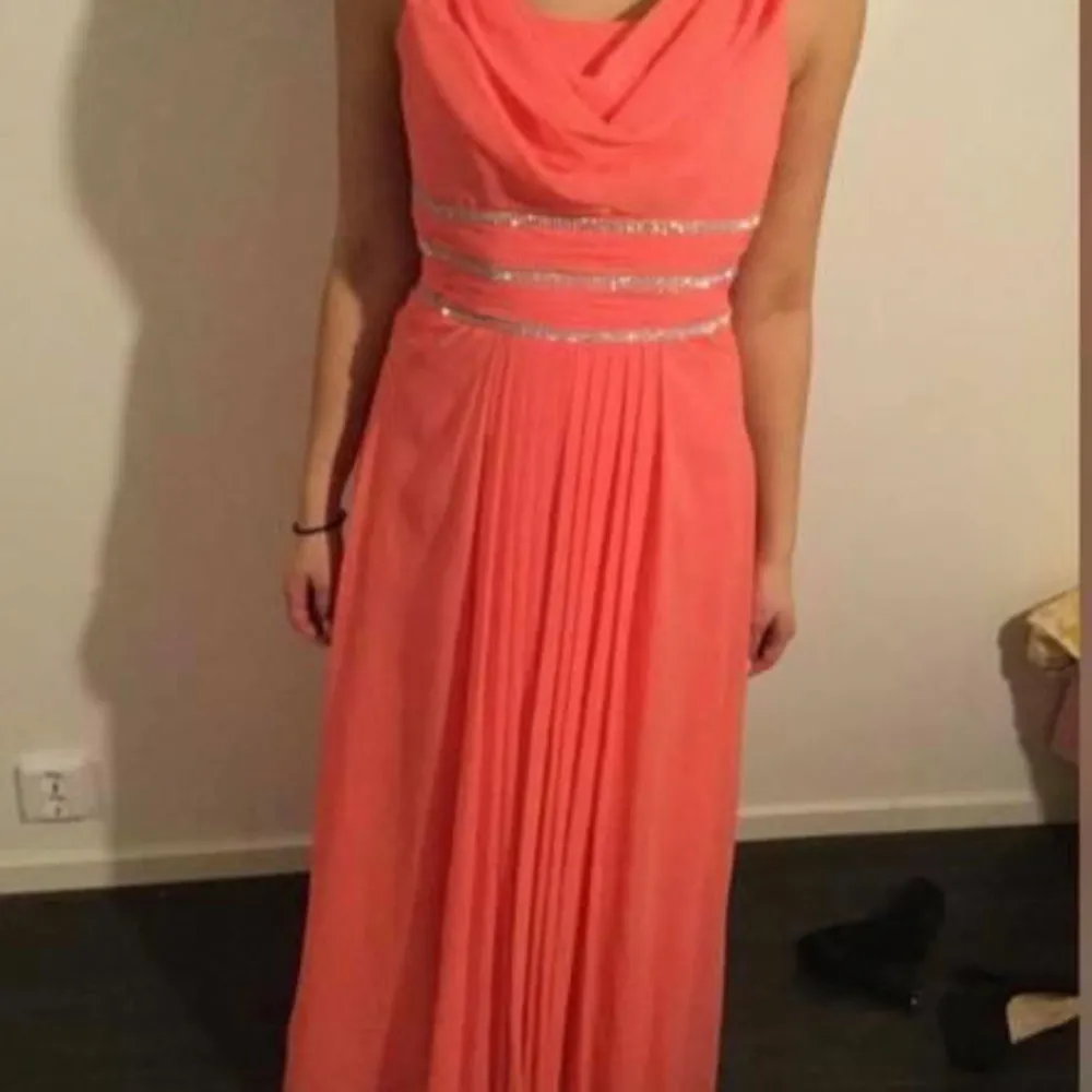 Elegant korallfärgad långklänning med glittriga band i midjan. Klänningen har en draperad halslinje och är ärmlös, vilket ger en stilren look. Perfekt för speciella tillfällen.finns i norsborg botkyrka . Mekot.