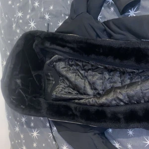 Svart moose knuckles jacka - Snygg svart jacka från Moose knuckles med fuskpälsfoder och dragkedja. Jackan har en huva och en cool logga på ärmen. Perfekt för kyliga dagar.