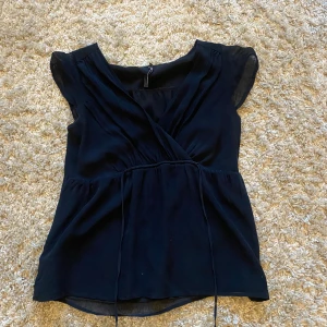 Omlott topp - Säljer en elegant svart omlottopp med korta ärmar. Toppen har en v-ringad design och knytband i midjan för en smickrande passform😘