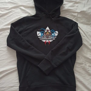 Svart hoodie från adidas med spindeltryck - Säljer en svart hoodie från Adidas med ett unikt spindeltryck på framsidan. Använd fåtal gånger så den är perfekt skick. Storlek M